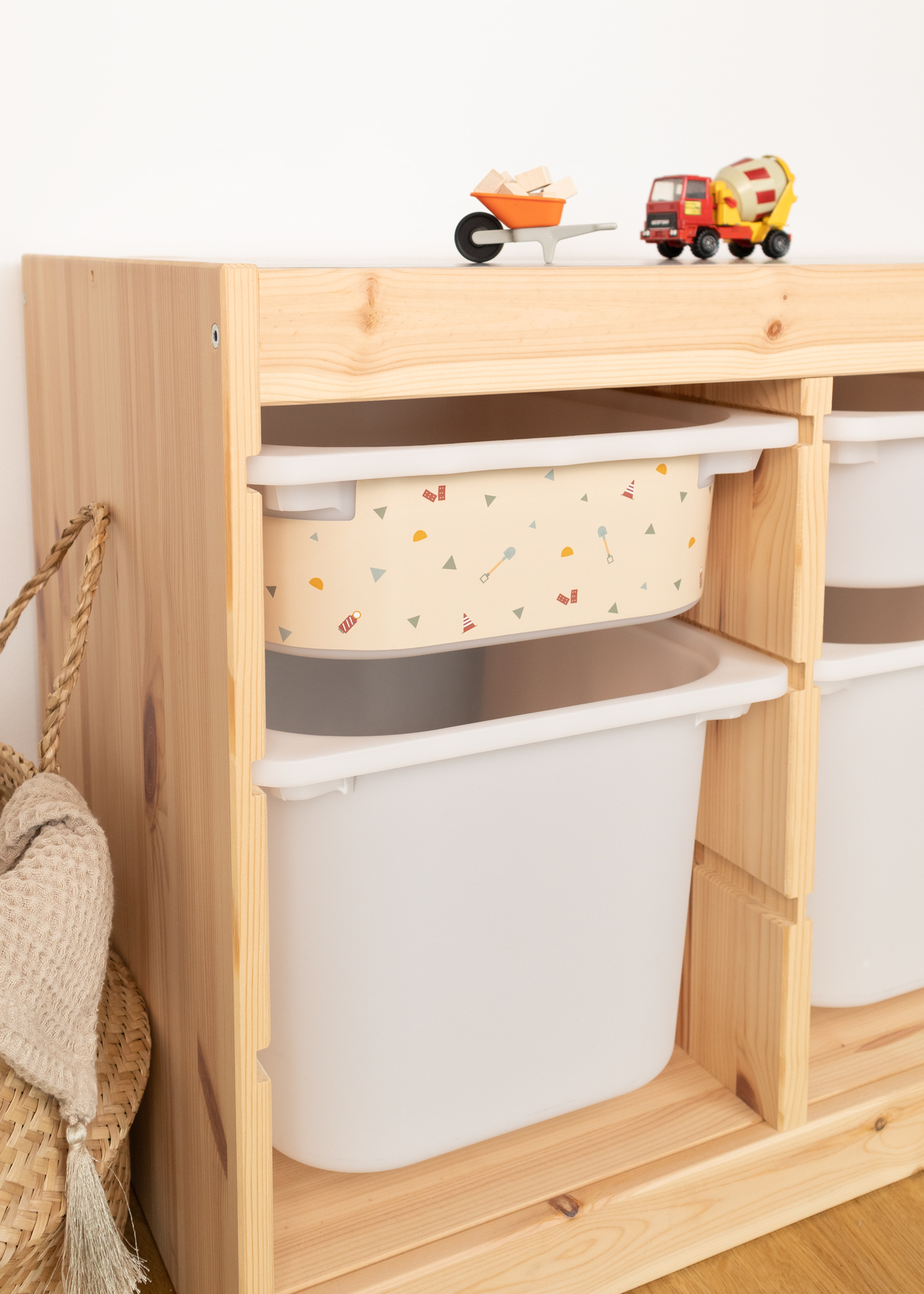 Seitliche Ansicht des IKEA TROFAST Regals mit einer kleinen beige Aufbewahrungsbox, dekoriert mit Motiven von Bagger, Kran und Kipplader, kombiniert mit einer großen weißen Box darunter.