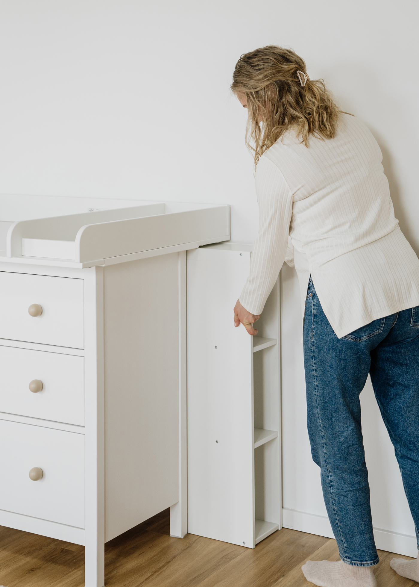 eine Frau schiebt ein weißes Regal hinter die Ikea Hemnes mit Wickelaufsatz 