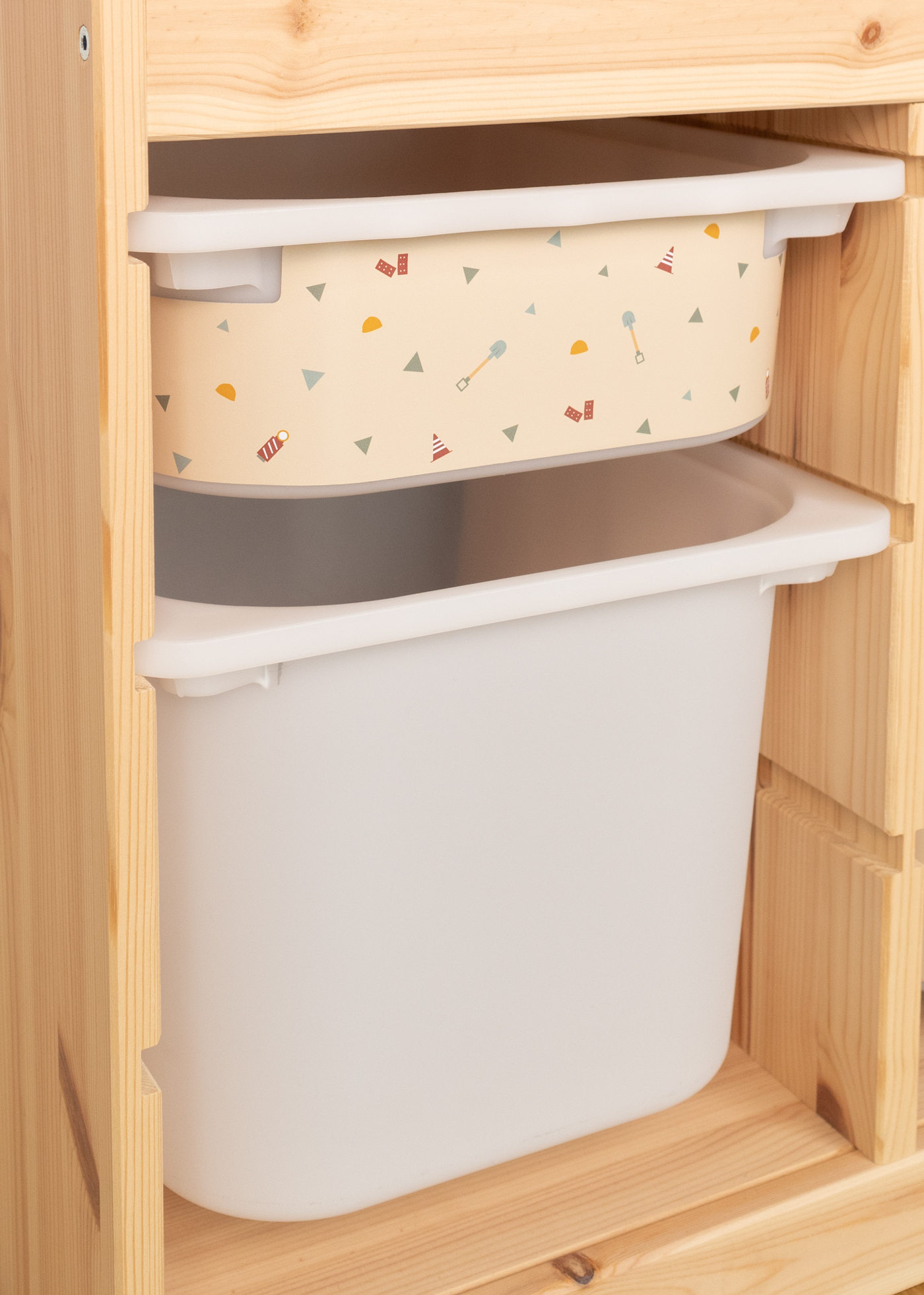 Baustellen-Motive auf Aufbewahrungsbox im TROFAST Regal IKEA TROFAST Regal mit kindgerechter Aufbewahrungsbox, die beige beklebt ist und Bagger-, Kran- und Kippladermotive zeigt, ideal für Kinderzimmer.