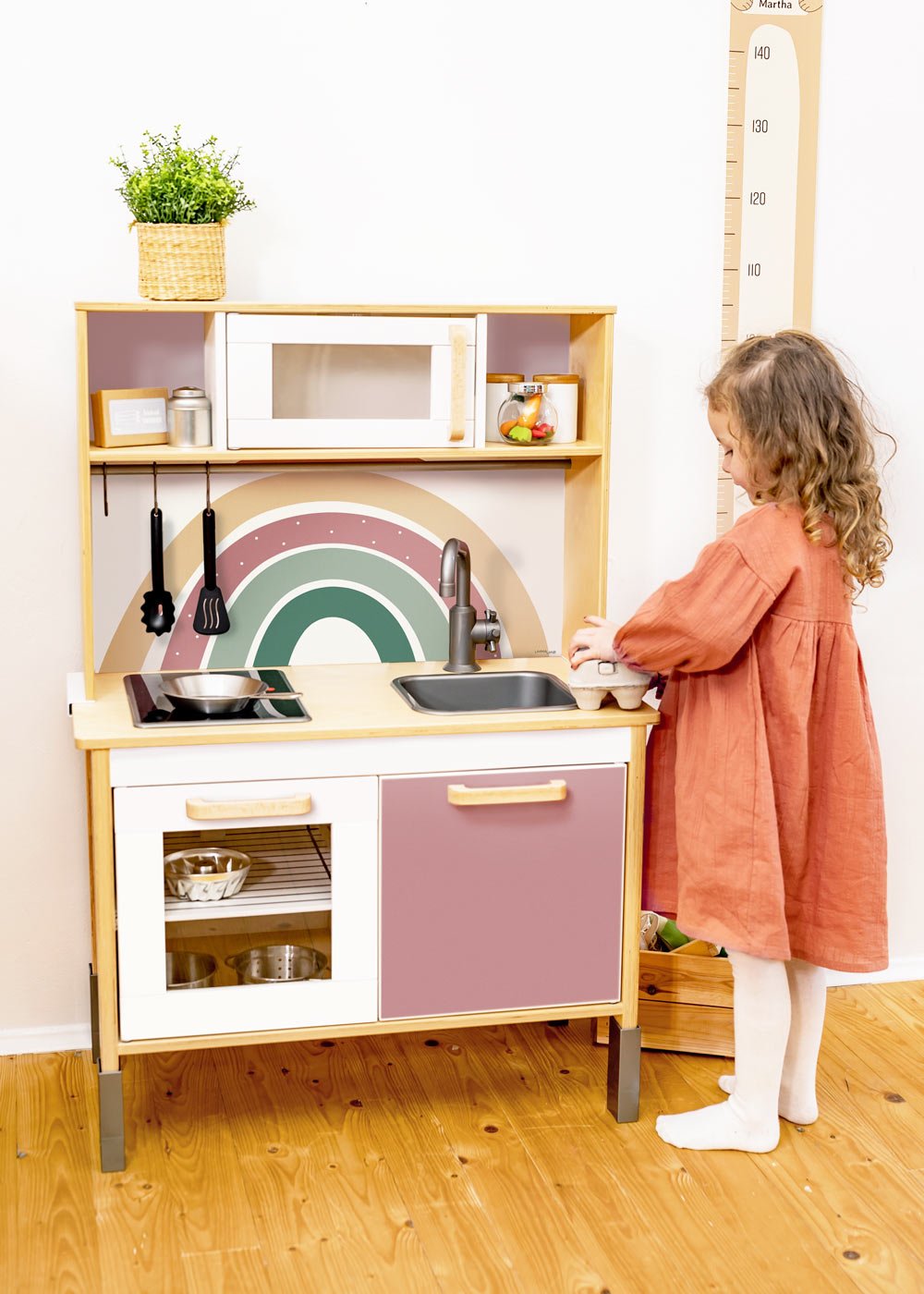 Limmaland Regenbogen Klebefolie Ein Mädchen smit rotem Kleid steht vor einer Ikea Duktig Kinderküche, welche mit Klebefolien mit Regenbogenmotiven von Limmaland beklebt ist